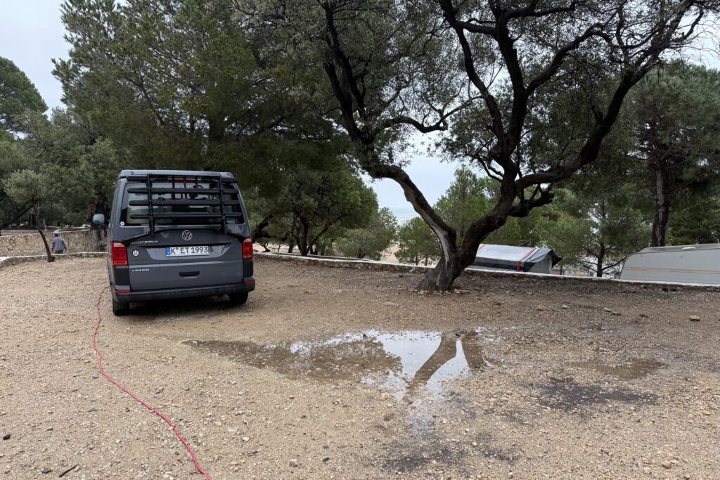 Der VW Bus auf dem Stellplatz hinter einer Regenpfütze