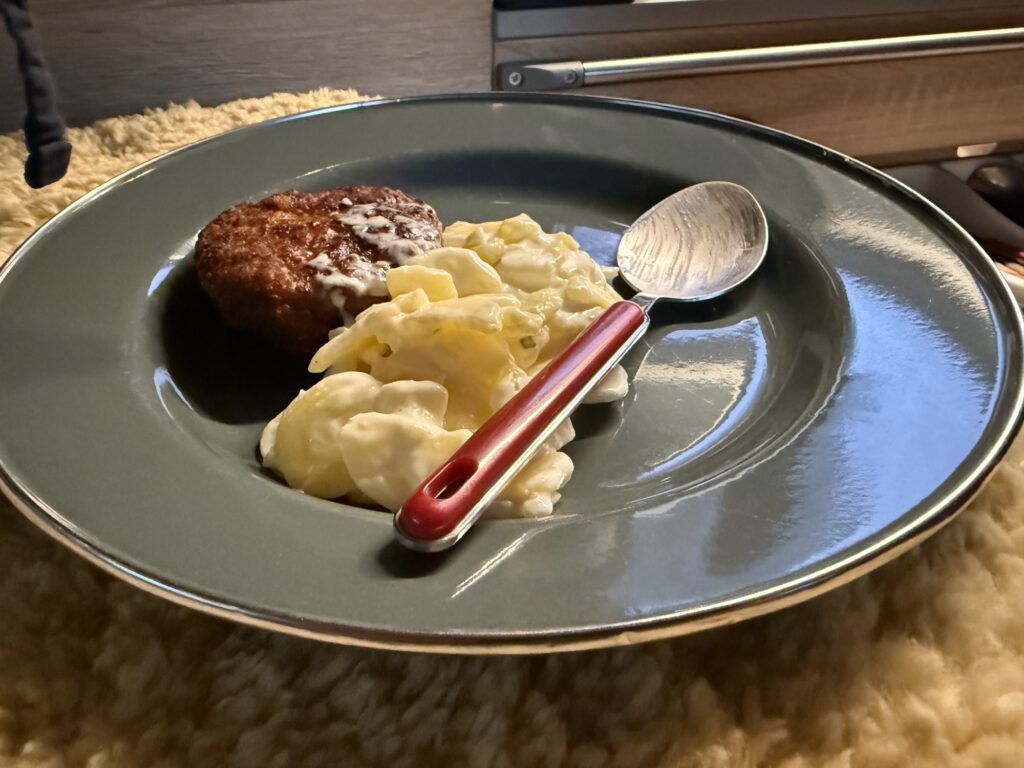 Teller mit einer warmen Frikadelle mit Kartoffelsalat und einem Löffel